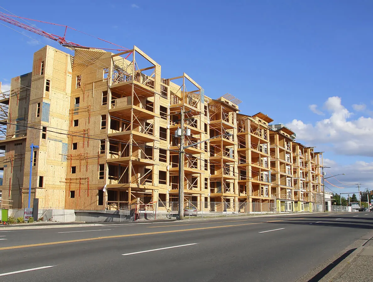 Wooden apartment building under construction, clear sky.